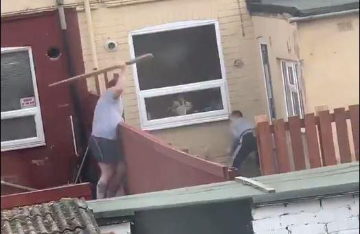 two neighbours throwing planks of wood at each other other their fence